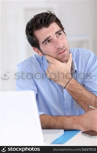 Office worker with thoughtful look in front of laptop