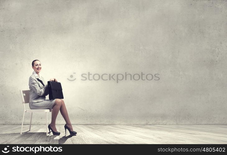 Office worker. Young businesswoman sitting in chair with suitcase in hands