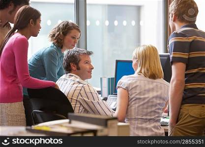 Office workers standing around colleague using computer back view