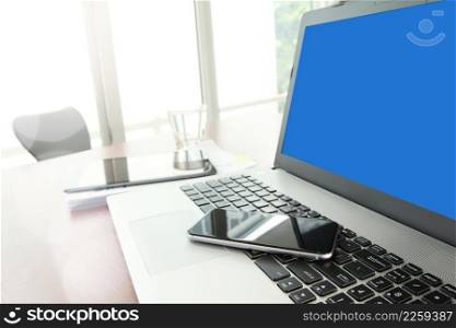 Office workplace with blank screen laptop computer and smart phone and stylus with digital tablet on wood table