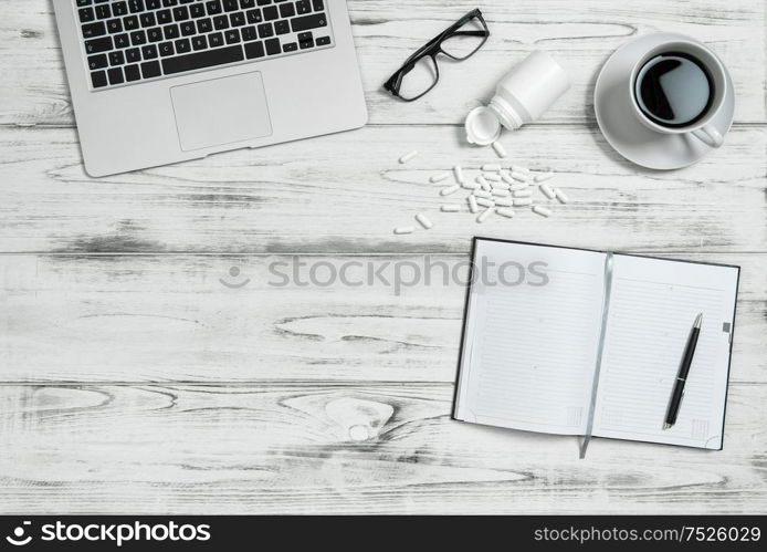 Office workplace with calendar book, cup of coffee, computer and medicine capsules. Stress and tiredness concept. Blue toned picture