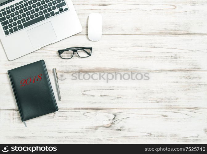 Office workplace with laptop, calendar book and glasses on wooden table. New Year goals 2018