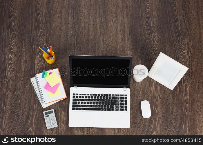 Office workplace with office supplies and laptop. Laptop and office supplies on the wooden table as seen from above