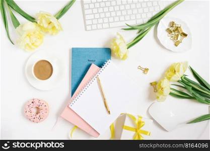 Office workspace with a white desk. Top view from above with a keyboard, notepad, gift, flowers and pencil with a white cup of coffee on a plate. Flat surface with copy space. Women’s business concept