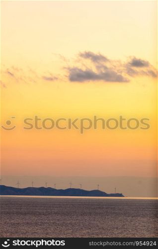 Offshore power generators farm at sunset. Scenic sea landscape with wind turbines, Greece. Renewable eco energy concept.. Sea view with wind turbines farm at sunset