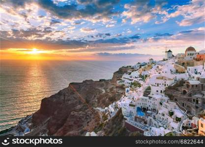 Oia or Ia at sunset, Santorini, Greece. Picturesque view, Old Town of Oia or Ia on the island Santorini, white houses, windmills and church with blue domes at sunset, Greece