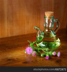 Oil and flowers of milk thistle on wooden background/