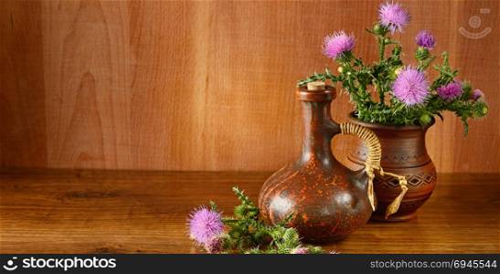 Oil and flowers of milk thistle on wooden background. Wide photo.