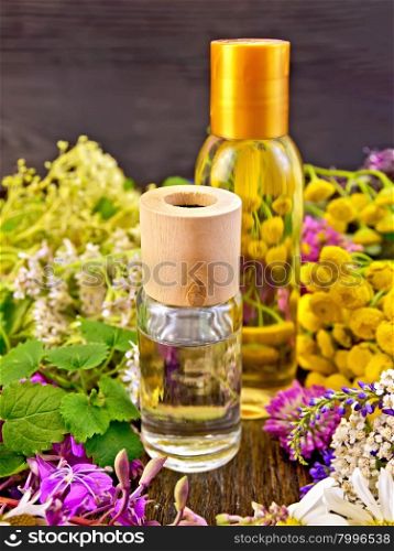 Oil and lotion bottles, fireweed flowers, tansy, chamomile, clover, yarrow and meadowsweet, mint leaves on a dark wooden board