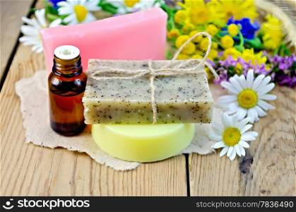Oil in a bottle, homemade soap on a piece of paper, chamomile flowers, tansy, elecampane on the background of wooden boards