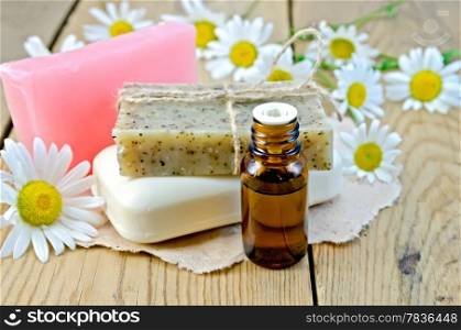 Oil in a bottle, homemade soap on a piece of paper, daisy flowers on a background of wooden boards