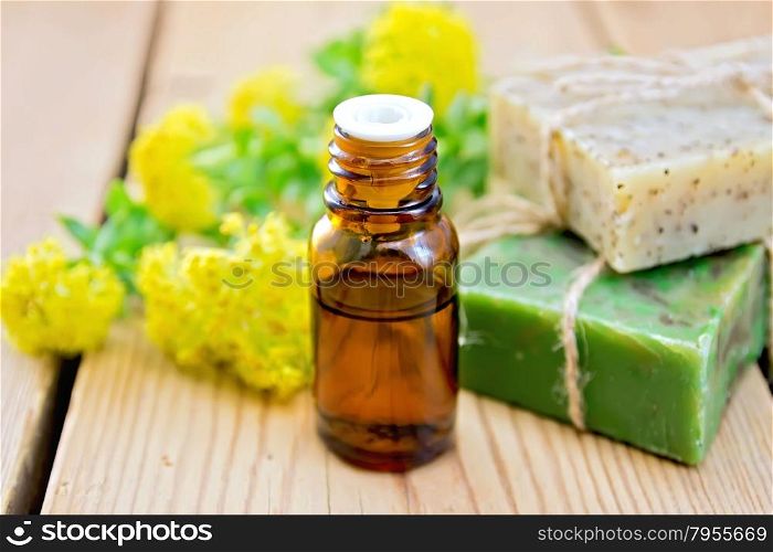 Oil in a bottle, two bars of homemade soap, flowers and leaves of Rhodiola rosea on a wooden boards background