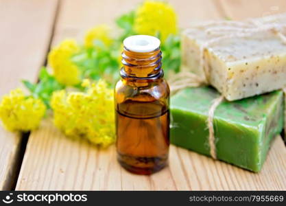 Oil in a bottle, two bars of homemade soap, flowers and leaves of Rhodiola rosea on a wooden boards background