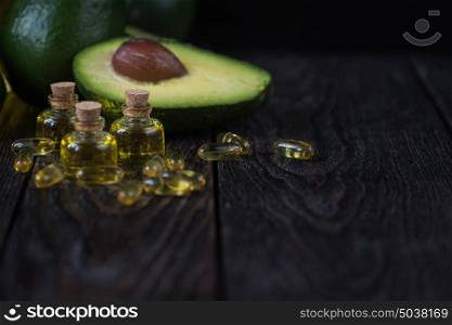 Oil of avocado and fish oil. Oil of avocado with fish oil pills on a dark wooden background