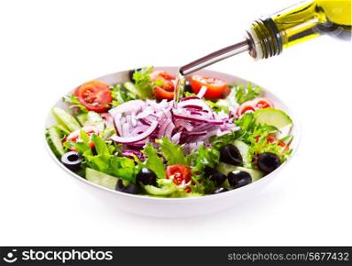oil pouring into bowl of salad on white background
