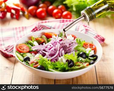 oil pouring into bowl of salad on wooden table