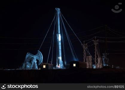 Oil pump jack and drilling rig at the night sky background. Oil fields in Western Siberia.