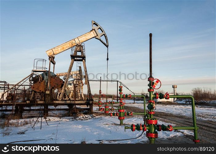 Oil pump jack and wellhead in the oilfield. Oil pump jack and wellhead in the oilfield. Oil and gas concept.