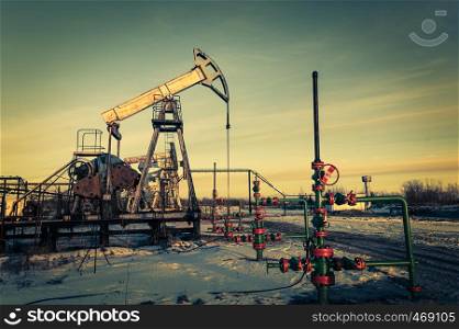 Oil pump jack and wellhead on an oil field. Mining and petroleum industry. Power generation concept. Oil and gas industry theme.. Oil pump jack and wellhead on an oil field. Mining and petroleum industry. Power generation concept.