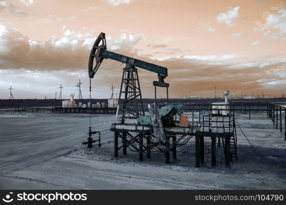 Oil pump jack and wellhead with valve armature during sunset on the oilfield. Extraction of oil. Oil and gas concept. Toned.