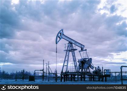Oil pump jack and wellhead with valve armature during sunset on the oilfield. Extraction of oil. Oil and gas concept. Toned.