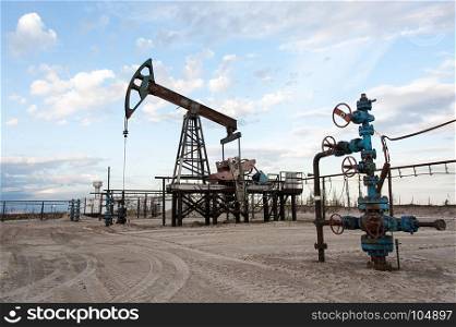 Oil pump jack and wellhead with valve armature during sunset on the oilfield. Extraction of oil. Oil and gas concept.