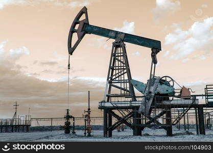 Oil pump jack and wellhead with valve armature during sunset on the oilfield. Extraction of oil. Oil and gas concept. Toned.