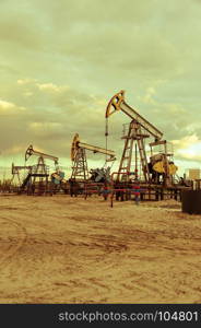 Oil pump jacks group and wellhead with valve armature during sunset on the oilfield. Oil and gas concept. Dramatic cloudy sky background. Toned.