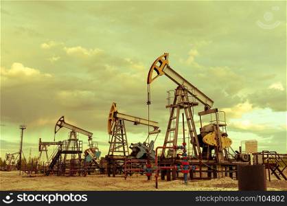 Oil pump jacks group and wellhead with valve armature during sunset on the oilfield. Oil and gas concept. Dramatic cloudy sky background. Toned.