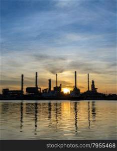 Oil refinery or petrochemical industry plant at sunrise in silhouette view with reflection