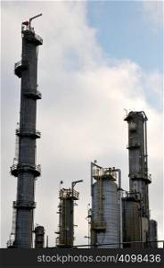 Oil refinery stacks tower against a cloudy blue sky.