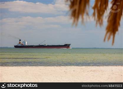 Oil tanker sailing past empty tropical beach with palm tree and white sand