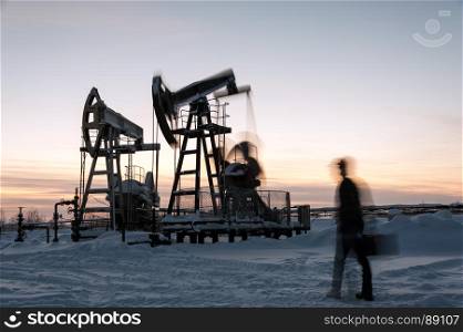 Oil worker in a oilfield. Pump jack and engineer on a winter sunset sky background. Western Siberia. Blurred motion.