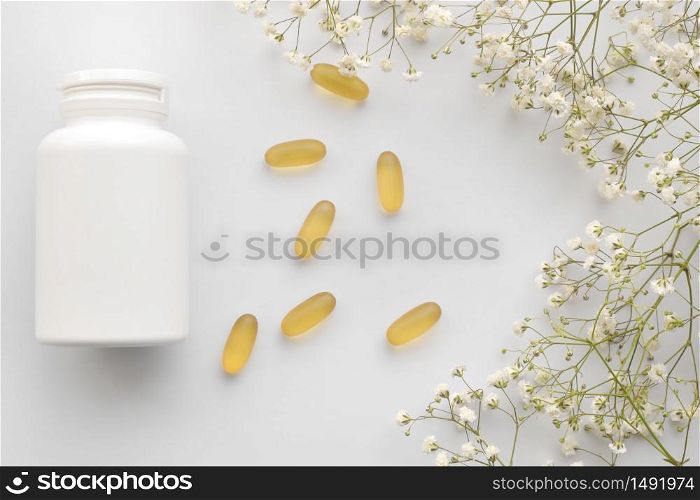 Oil yellow gelatin capsules with white bottle on white background with flowers, vitamins and antioxidant concept Omega 3, liver cod or evening primose oil for healthcare. Minimalism. Copy space. Oil yellow gelatin capsules with white bottle on white background with flowers, vitamins and antioxidant concept Omega 3, liver cod or evening primose oil for healthcare. Minimalism. Copy space.