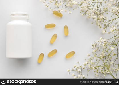 Oil yellow gelatin capsules with white bottle on white background with flowers, vitamins and antioxidant concept Omega 3, liver cod or evening primose oil for healthcare. Minimalism. Copy space. Oil yellow gelatin capsules with white bottle on white background with flowers, vitamins and antioxidant concept Omega 3, liver cod or evening primose oil for healthcare. Minimalism. Copy space.