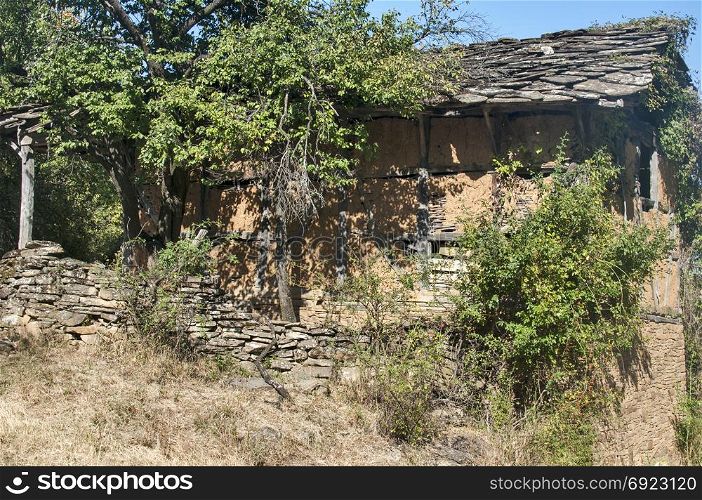 Old abandoned crumbling adobe ramshackle rickety house with stone slabs roof in late summer