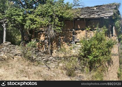 Old abandoned crumbling adobe ramshackle rickety house with stone slabs roof in late summer