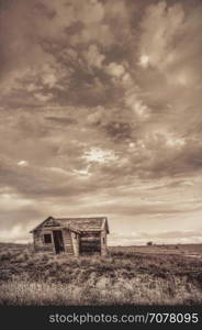 old abandoned farm house on Colorado prairie with stormy sky, sepia toning