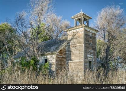 old abandoned schoolhouse in rural Nebraska overgrown by trees and weeds