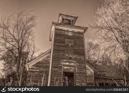 old abandoned schoolhouse in rural Nebraska overgrown by trees and weeds, sepia toned image