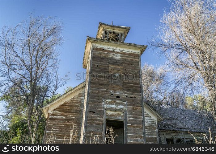 old abandoned schoolhouse with a bell tower in rural Nebraska overgrown by trees and weeds