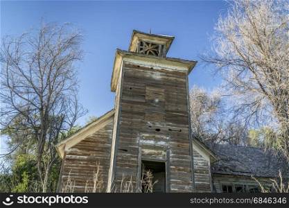 old abandoned schoolhouse with a bell tower in rural Nebraska overgrown by trees and weeds
