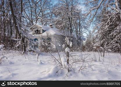 Old abandoned white wooden house among snow-covered trees on a frosty winter day.