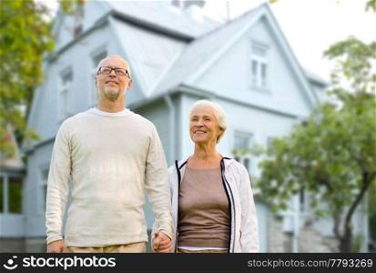old age, accommodation and real estate concept - happy senior couple holding hands over living house background. happy senior couple holding hands over house