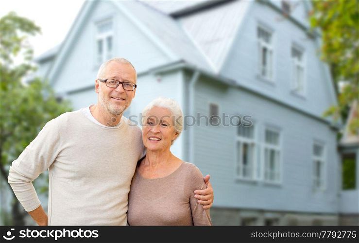 old age, accommodation and real estate concept - happy senior couple hugging over house background. happy senior couple hugging over house background