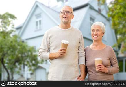 old age, accommodation and real estate concept - happy senior couple with coffee cups holding hands over living house background. happy senior couple with coffee over living house