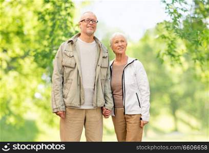 old age and people concept - happy senior couple holding hands over green natural background. happy senior couple over green natural background