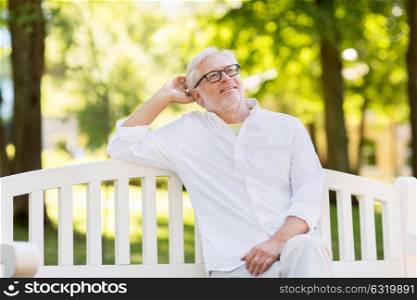 old age and people concept - happy senior man in glasses sitting at summer park. happy senior man in glasses sitting at summer park