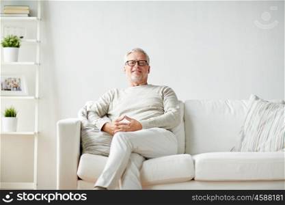 old age, comfort and people concept - smiling senior man in glasses sitting on sofa at home