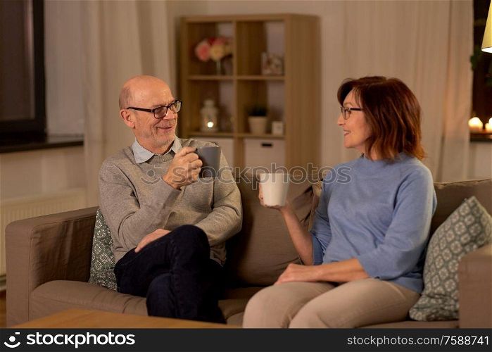 old age, drink and people concept - happy senior couple drinking tea at home in evening. happy senior couple drinking tea at home at night